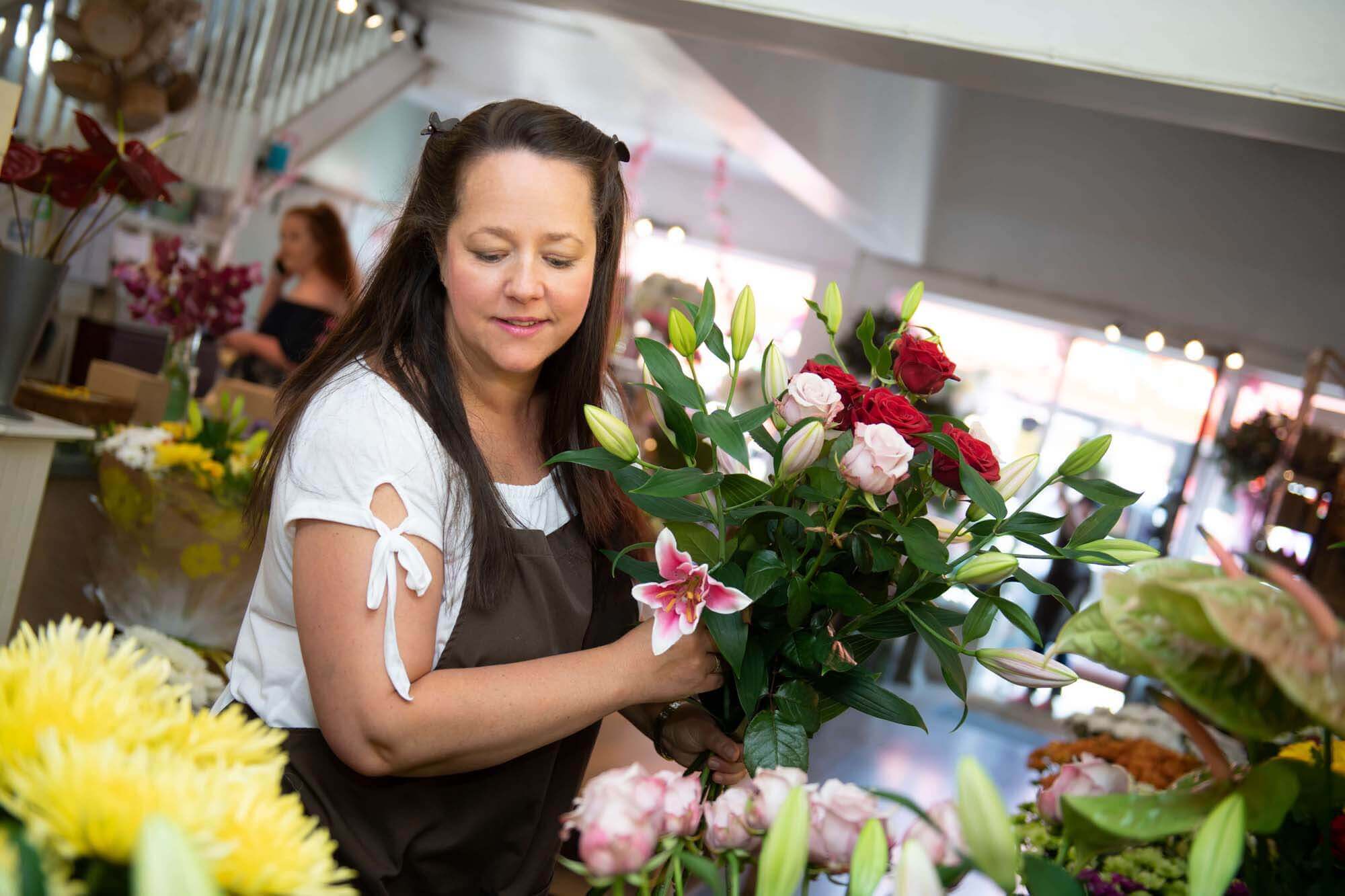 Local florist arranging fresh bouquet of red roses, pink lilies and buds for same-day flower delivery in the UK