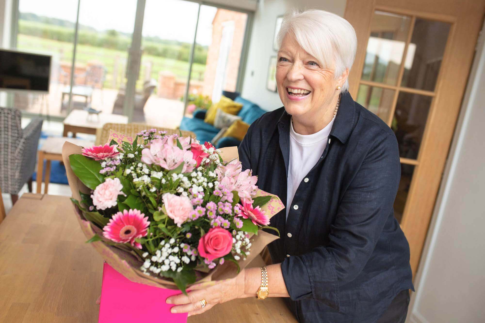 Lady smiling and placing beautiful bouquet of fresh pink, cerise and white flowers on a table